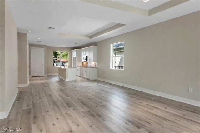 unfurnished living room with light hardwood / wood-style flooring and a tray ceiling