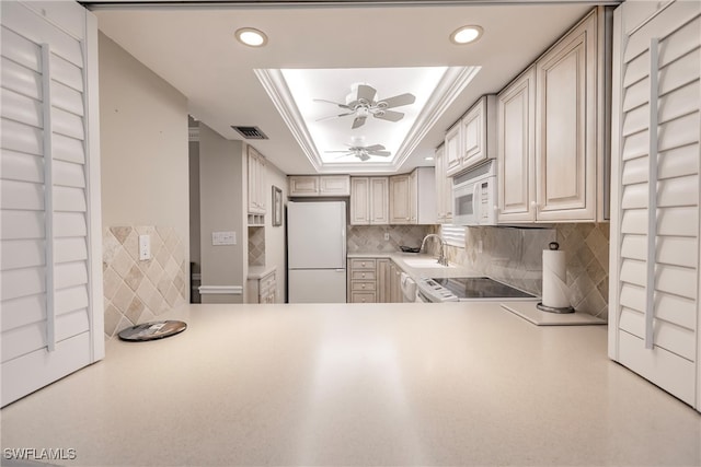 kitchen with a raised ceiling, sink, white appliances, and ceiling fan