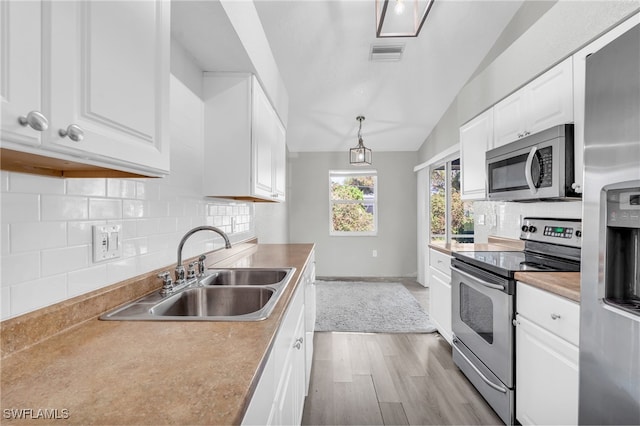 kitchen featuring white cabinetry, appliances with stainless steel finishes, pendant lighting, lofted ceiling, and light wood-type flooring