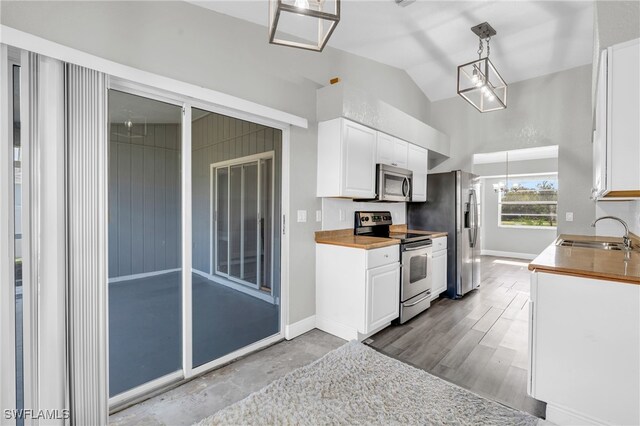 kitchen with white cabinetry, appliances with stainless steel finishes, decorative light fixtures, sink, and lofted ceiling