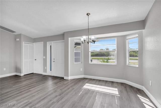 unfurnished dining area with hardwood / wood-style floors, a textured ceiling, and a chandelier