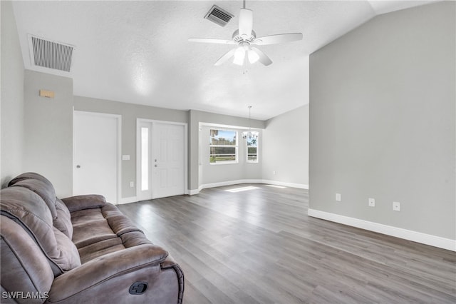 living room featuring hardwood / wood-style floors, ceiling fan with notable chandelier, lofted ceiling, and a textured ceiling