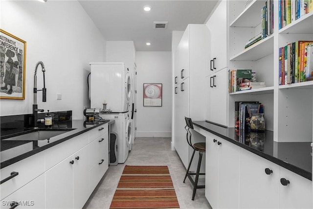 kitchen with a breakfast bar area, stacked washer / dryer, sink, and white cabinets