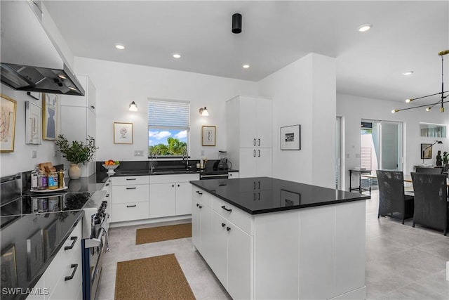 kitchen with wall chimney range hood, an inviting chandelier, white cabinets, a center island, and stainless steel electric range