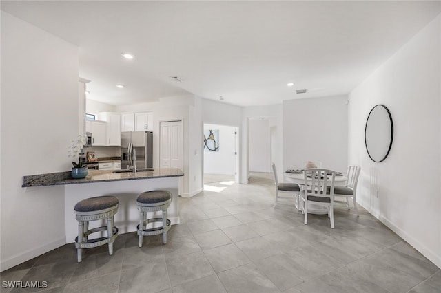 kitchen with white cabinetry, stainless steel appliances, kitchen peninsula, dark stone countertops, and a breakfast bar