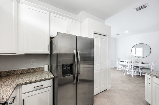 kitchen featuring dark stone countertops, stainless steel fridge, and white cabinets