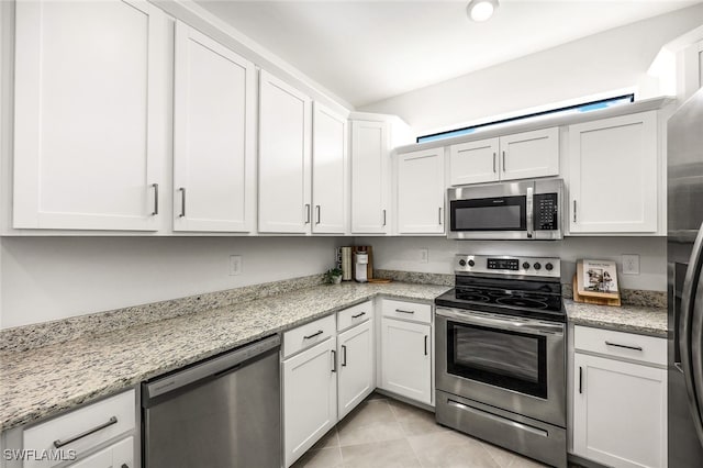 kitchen with light stone countertops, stainless steel appliances, white cabinetry, and light tile patterned flooring