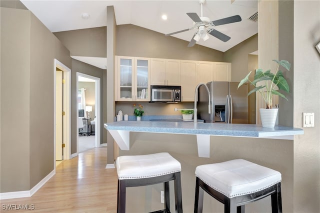 kitchen featuring kitchen peninsula, stainless steel appliances, a breakfast bar area, and vaulted ceiling