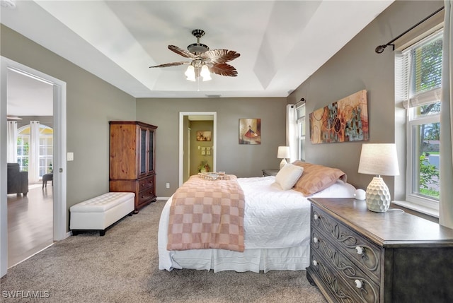 bedroom featuring light carpet, ceiling fan, and a tray ceiling