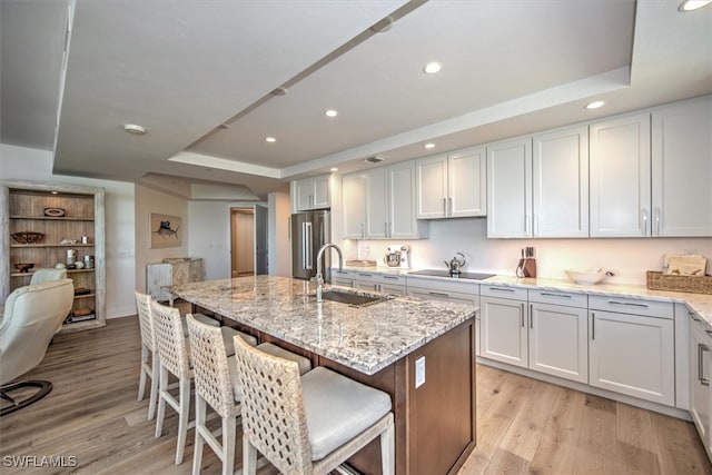 kitchen with stainless steel refrigerator, white cabinetry, a raised ceiling, and light wood-type flooring