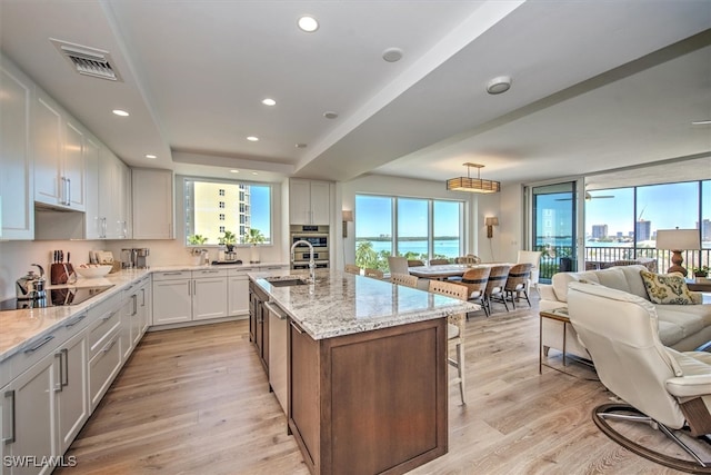 kitchen with white cabinetry, black electric stovetop, a center island with sink, and light wood-type flooring