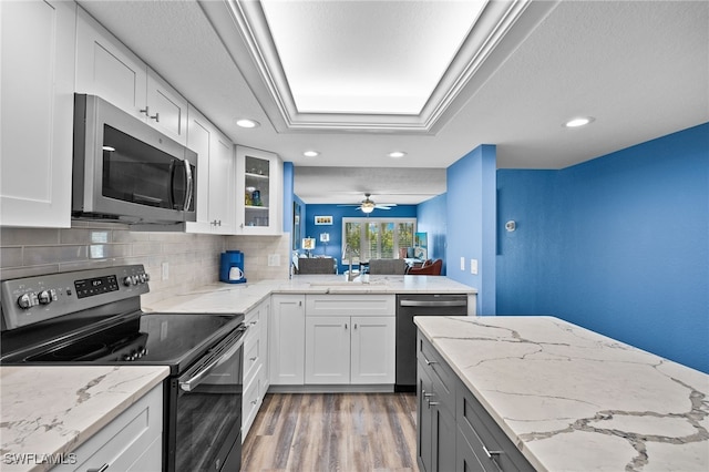 kitchen featuring stainless steel appliances, light stone counters, white cabinets, hardwood / wood-style floors, and ceiling fan