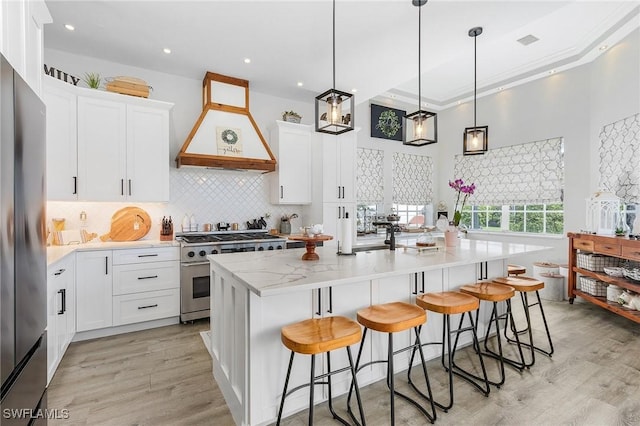 kitchen featuring premium range hood, white cabinets, an island with sink, and appliances with stainless steel finishes