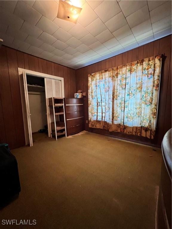 unfurnished bedroom featuring carpet flooring, a closet, and wood walls