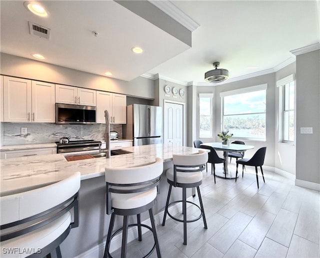 kitchen featuring light stone counters, tasteful backsplash, a breakfast bar, white cabinetry, and appliances with stainless steel finishes