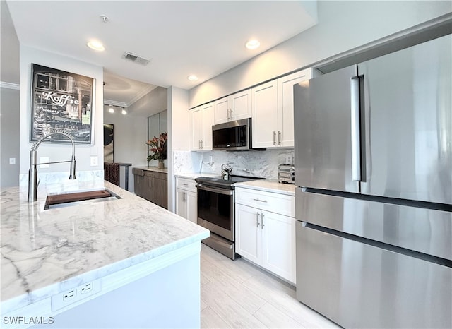 kitchen with stainless steel appliances, white cabinetry, sink, and light stone counters