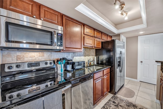 kitchen with appliances with stainless steel finishes, tasteful backsplash, a raised ceiling, and dark stone countertops