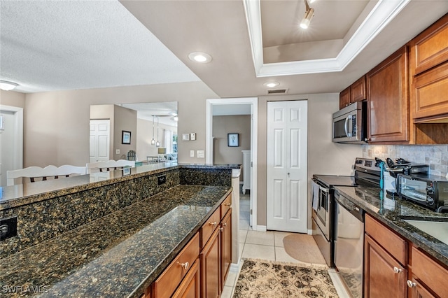 kitchen with stainless steel appliances, a textured ceiling, light tile patterned floors, decorative backsplash, and dark stone countertops