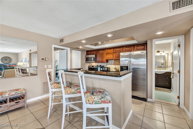 kitchen with a kitchen bar, dark stone counters, light tile patterned floors, tasteful backsplash, and appliances with stainless steel finishes