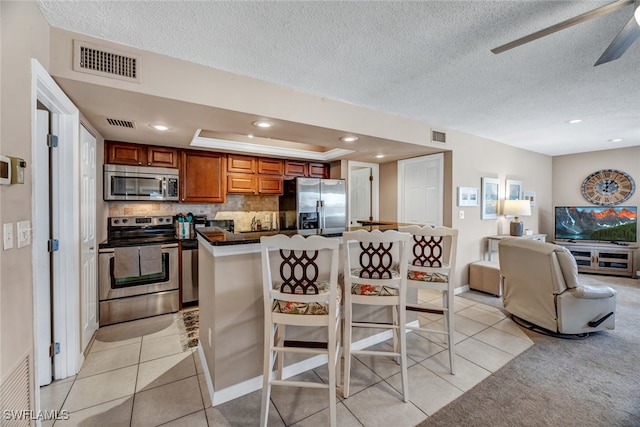 kitchen featuring stainless steel appliances, light tile patterned flooring, ceiling fan, backsplash, and a breakfast bar