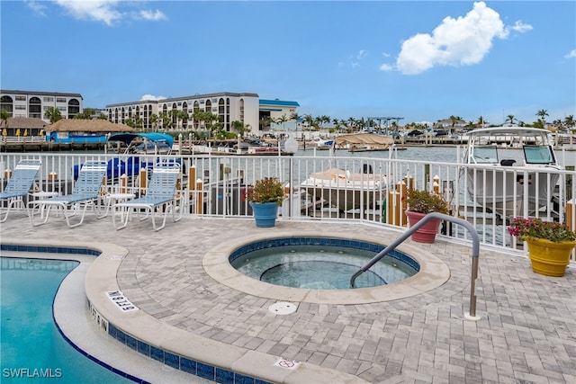 view of pool featuring a community hot tub, a water view, and a patio area