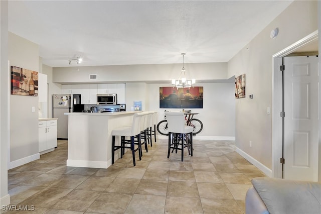 kitchen featuring stainless steel appliances, white cabinets, hanging light fixtures, a breakfast bar, and a notable chandelier