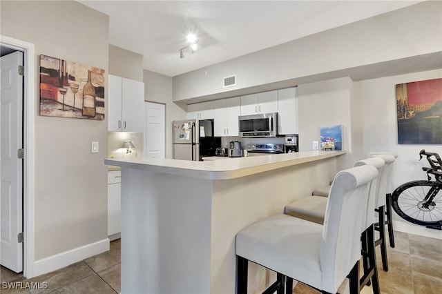 kitchen with kitchen peninsula, stainless steel appliances, white cabinets, light tile patterned flooring, and a kitchen breakfast bar