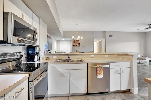 kitchen featuring pendant lighting, ceiling fan with notable chandelier, white cabinets, appliances with stainless steel finishes, and sink