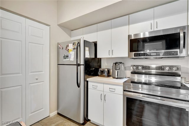 kitchen with appliances with stainless steel finishes, light tile patterned floors, light countertops, and white cabinetry