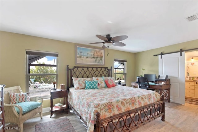 bedroom with hardwood / wood-style floors, a barn door, multiple windows, and connected bathroom