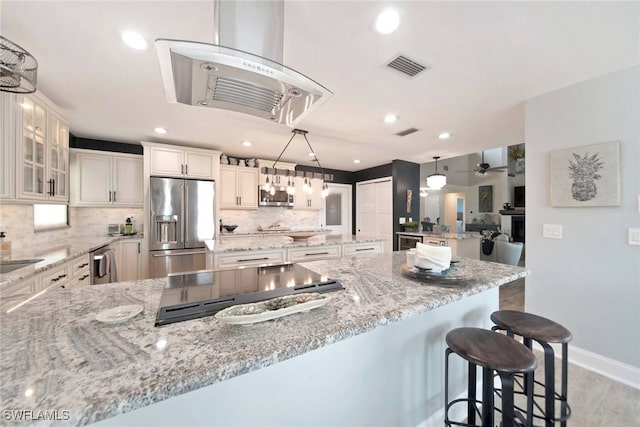 kitchen with backsplash, white cabinets, light stone countertops, appliances with stainless steel finishes, and decorative light fixtures