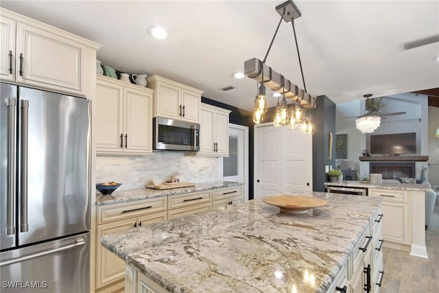 kitchen featuring light stone countertops, hanging light fixtures, stainless steel appliances, and cream cabinetry