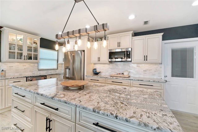 kitchen featuring white cabinets, decorative backsplash, light stone countertops, appliances with stainless steel finishes, and decorative light fixtures