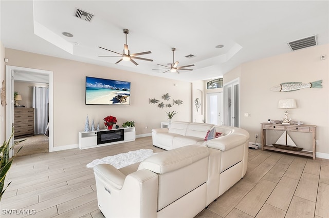 living room with ceiling fan, a raised ceiling, and light hardwood / wood-style flooring