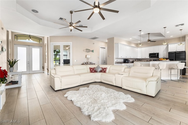 living room featuring french doors, light hardwood / wood-style floors, ceiling fan, and a raised ceiling