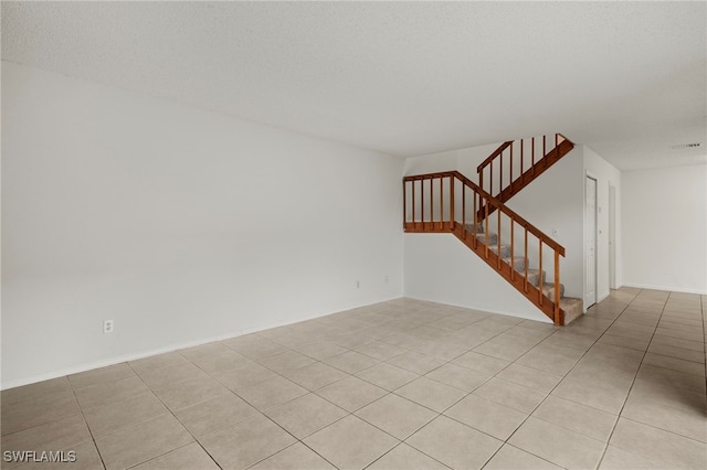 empty room featuring stairs, a textured ceiling, and light tile patterned flooring