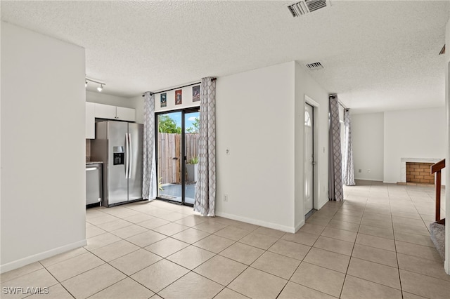 empty room with baseboards, visible vents, a textured ceiling, and light tile patterned flooring