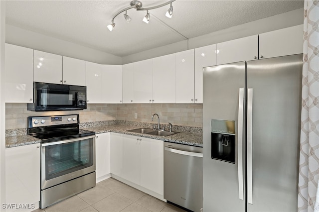 kitchen featuring light tile patterned floors, stainless steel appliances, a sink, white cabinets, and backsplash