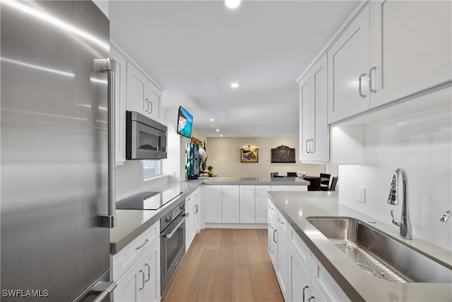 kitchen with stainless steel appliances, light hardwood / wood-style floors, white cabinets, kitchen peninsula, and sink