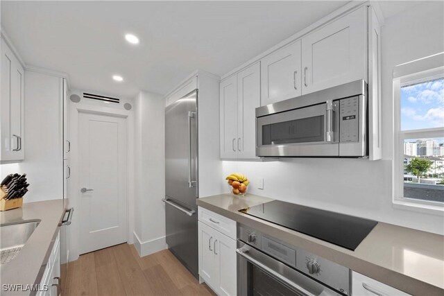 kitchen with light countertops, light wood finished floors, stainless steel appliances, white cabinets, and recessed lighting