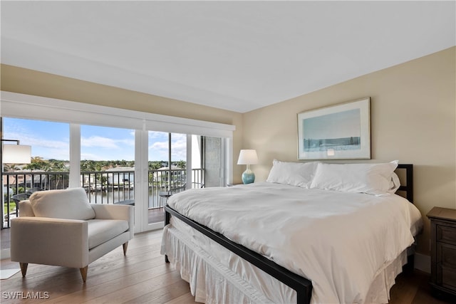 bedroom featuring light hardwood / wood-style floors, access to exterior, multiple windows, and a water view