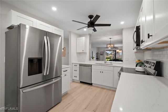 kitchen featuring appliances with stainless steel finishes, tasteful backsplash, decorative light fixtures, light hardwood / wood-style flooring, and white cabinets