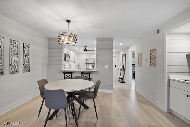 dining area with ceiling fan with notable chandelier and light hardwood / wood-style flooring