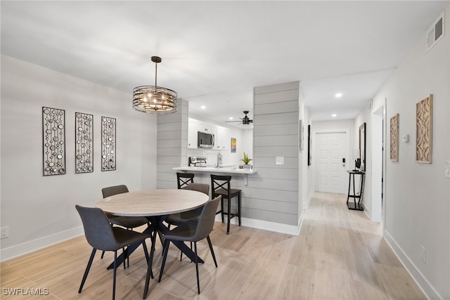 dining area featuring ceiling fan with notable chandelier and light hardwood / wood-style floors