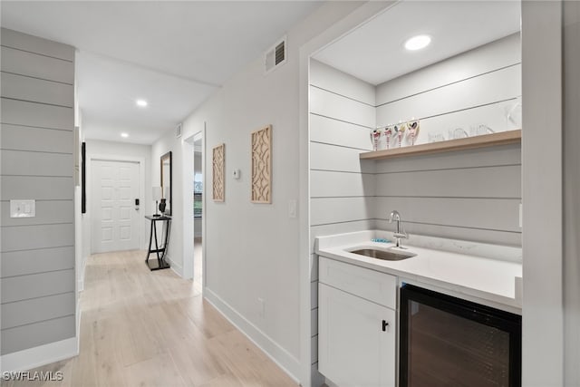 bar with white cabinets, light hardwood / wood-style flooring, wine cooler, and sink