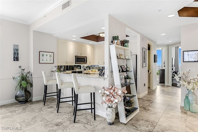 kitchen featuring crown molding, light stone counters, tasteful backsplash, a kitchen bar, and kitchen peninsula