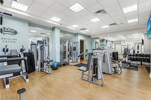 workout area with a paneled ceiling and light wood-type flooring