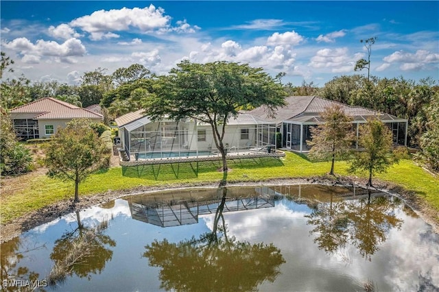 rear view of house featuring glass enclosure, a lawn, and a water view