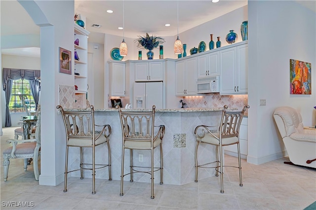 kitchen featuring kitchen peninsula, a breakfast bar area, white appliances, light stone countertops, and white cabinets