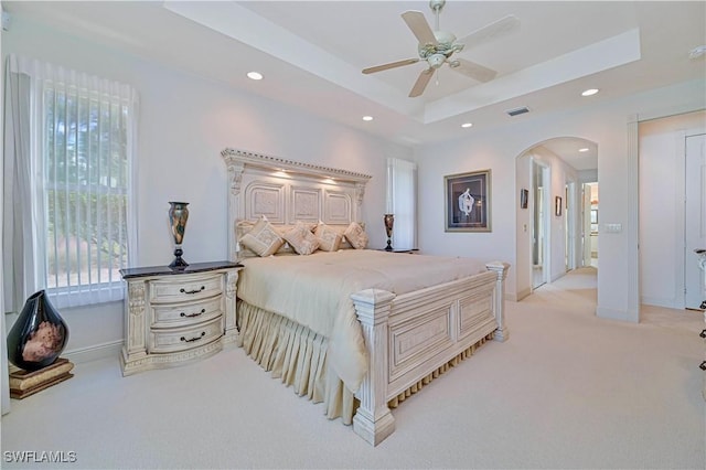 bedroom with ceiling fan, light colored carpet, and a tray ceiling